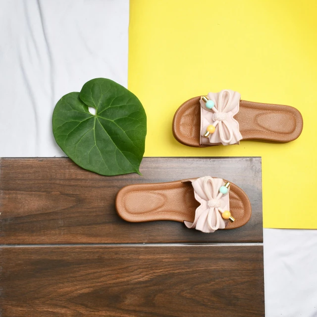 a pair of flip flops, one with a bow, the other with an embroidered ribbon, sit on top of a wooden box