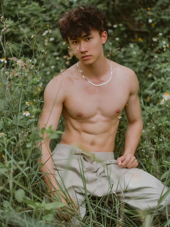 a shirtless young man sitting in a field of grass