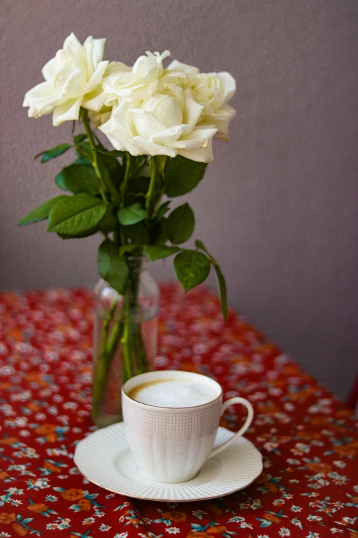 a cup and saucer with roses in a vase on a table