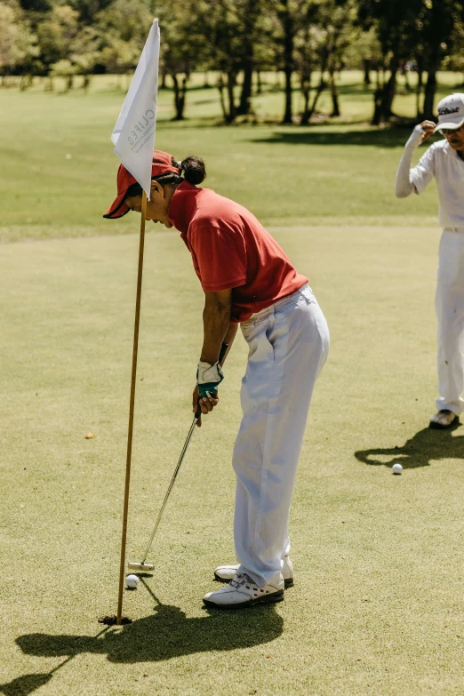 man wearing white pants and red shirt swinging a golf club