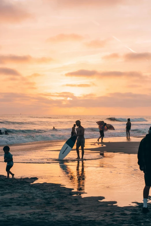 three people on the beach with a surfboard at sunset