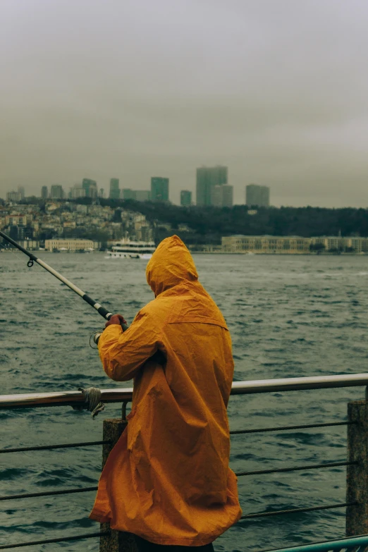 man in raincoat fishing on pier next to water