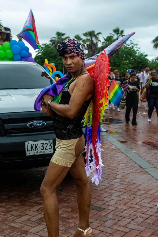 man in bikini top with rainbow kite in the street