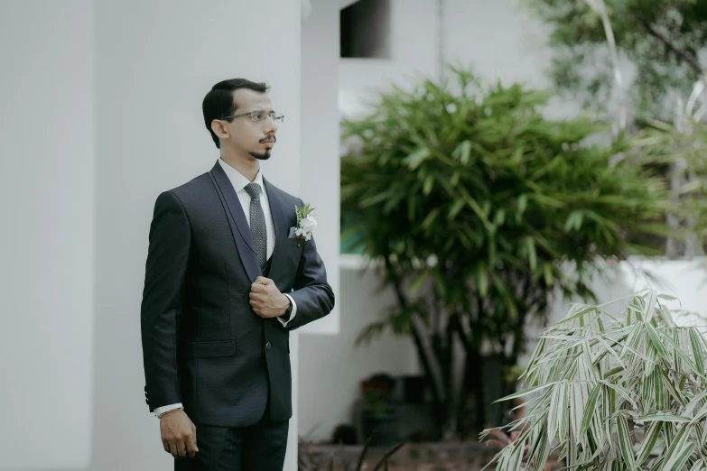 a man wearing a suit and tie while standing next to a potted plant