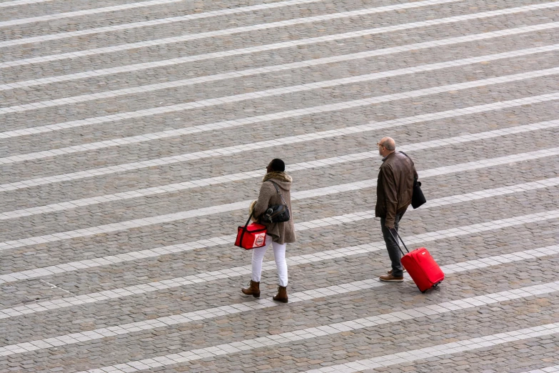 the man is walking next to the woman with two luggage bags