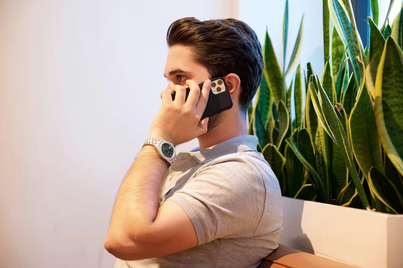 man with a watch on the phone while resting in front of some potted plants