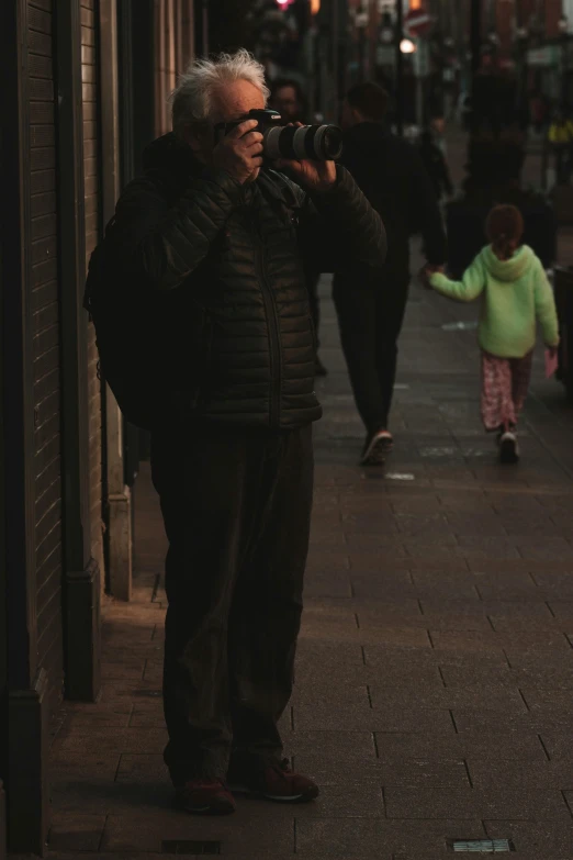 an elderly man standing on the side of a road holding a camera