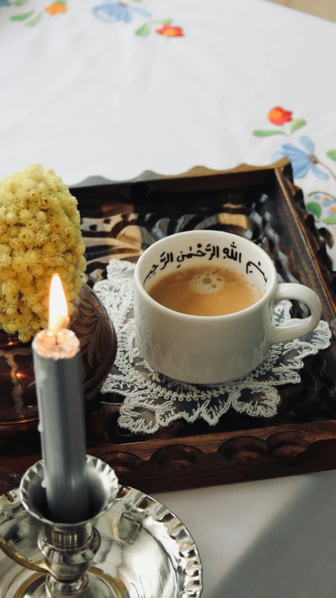 a cup of coffee on a tray near a lit candle