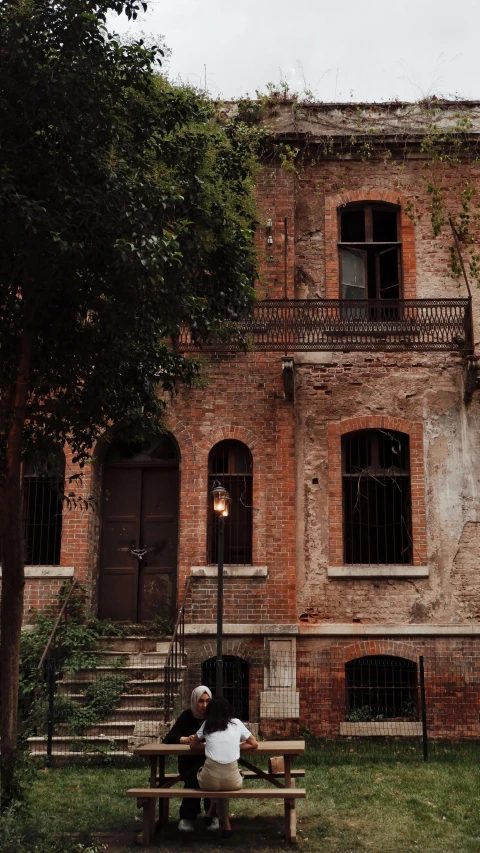 a man sits on a wooden bench in front of an old building