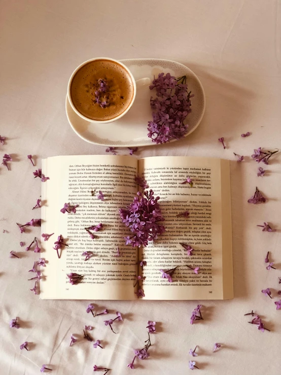 a book, coffee cup and flowers on a bed