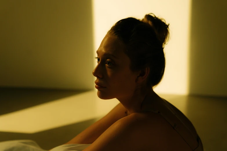 a woman with dark hair sitting down next to a wall