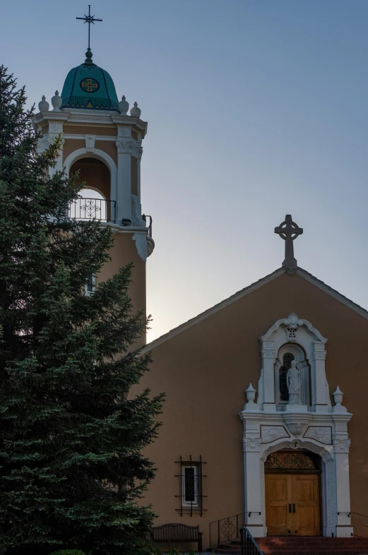 a church tower with a cross on top next to a pine tree