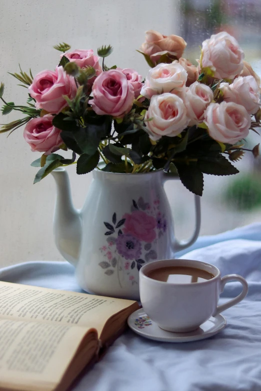 the table is set with a cup of coffee, a teapot and a bouquet of roses