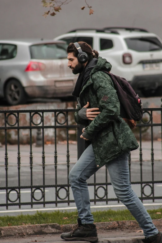 man walking along sidewalk near park with ear muffs