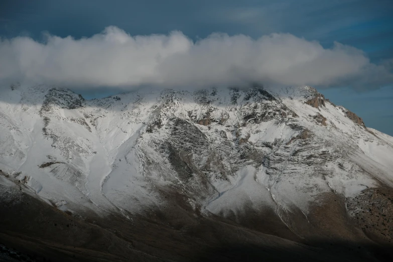 clouds hovering over the top of mountains covered in snow