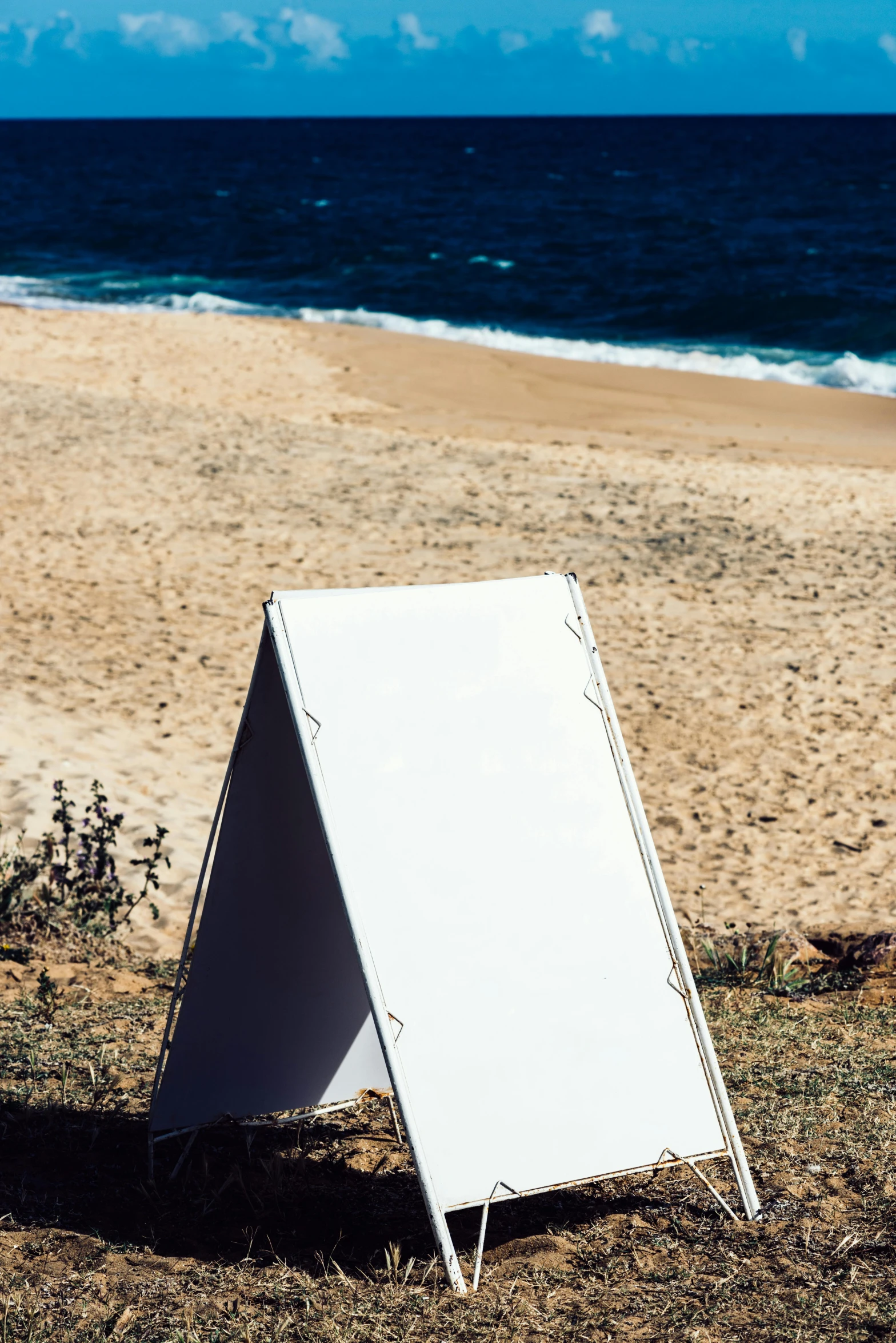 a sign sitting on the sand next to the ocean