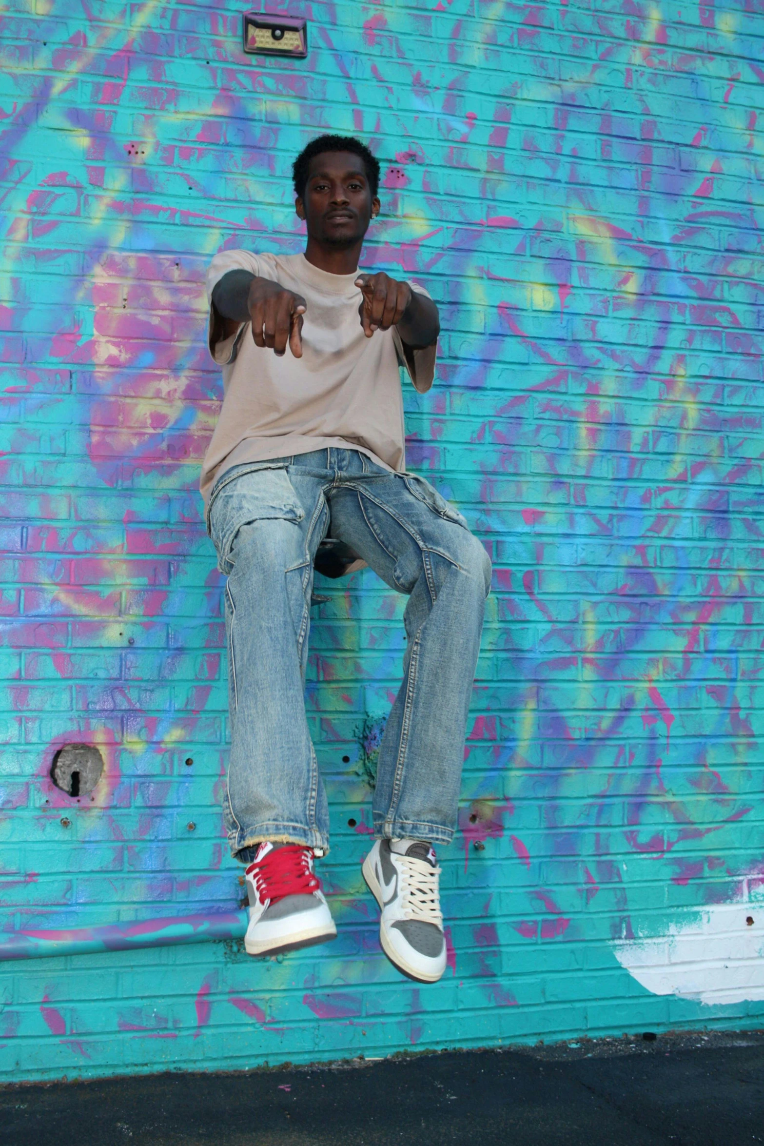 man posing on the graffiti wall pointing to camera