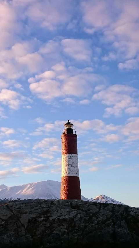 a lighthouse at the top of a cliff with mountains in the background