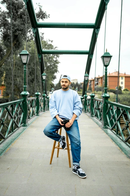 an african american man sitting on a small stool under a green bridge