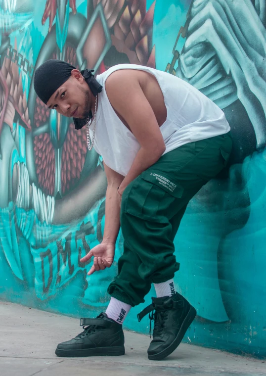 a man in a white shirt and green pants stands next to a blue wall