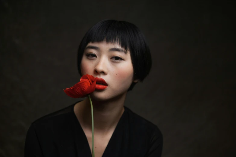 woman in black with red flower standing near black background