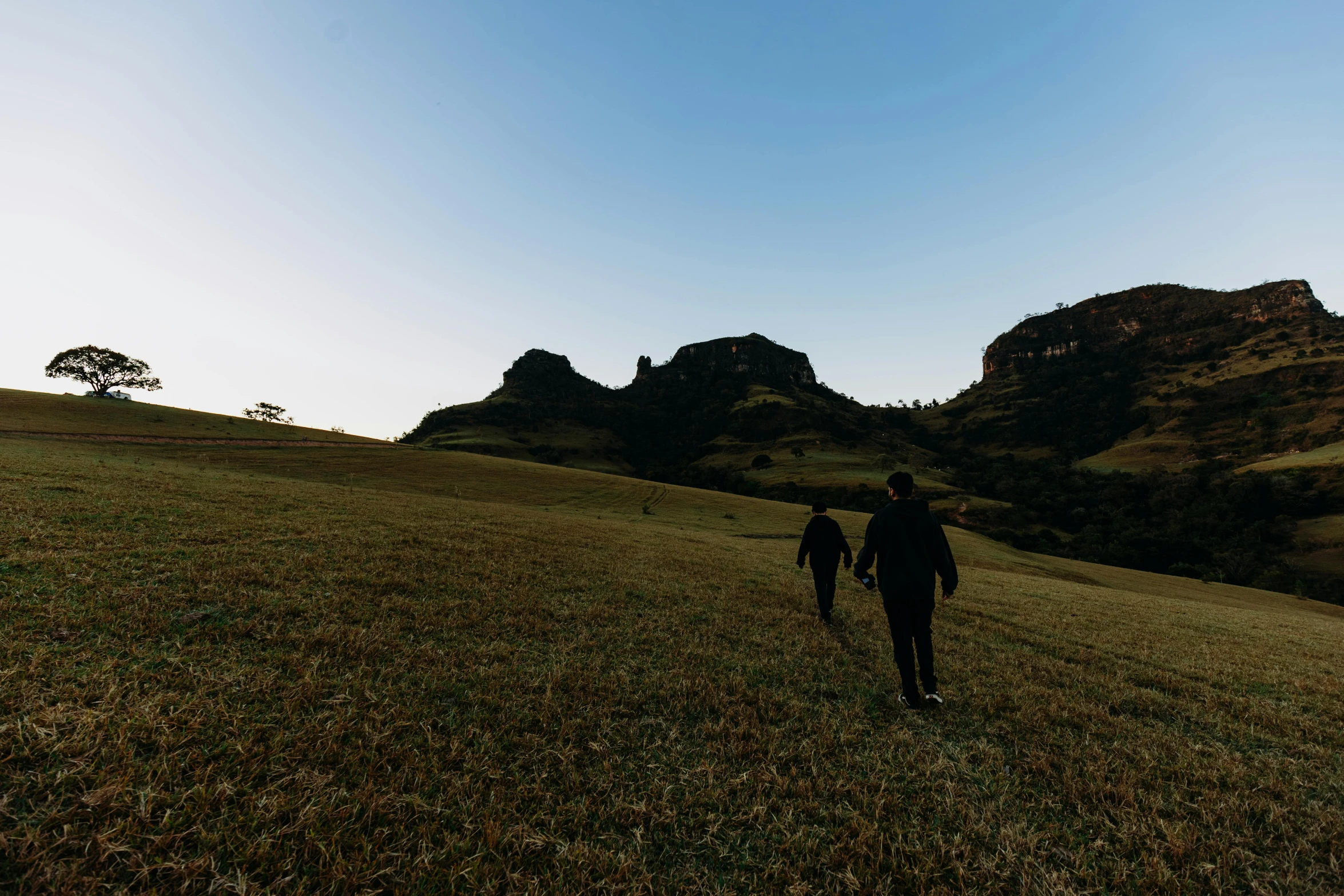 two people walk across an expansive field with grassy hills in the distance