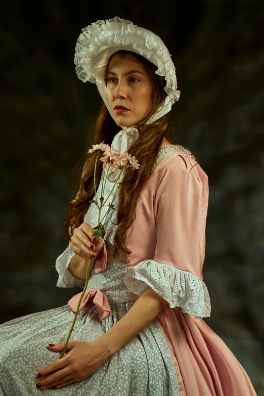 a woman wearing pink dress and hat holding a pink flower