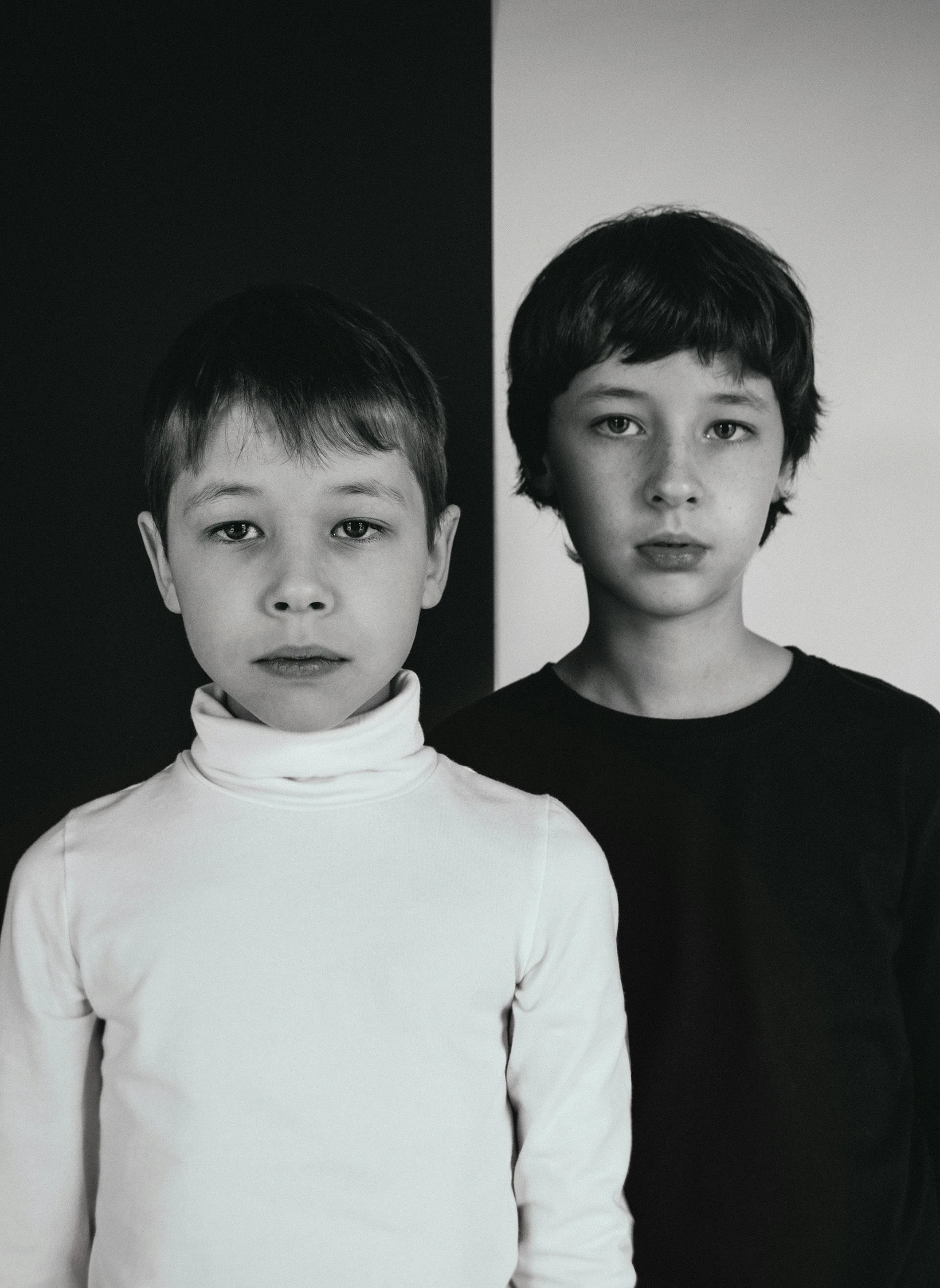 two young children stand in front of a white wall