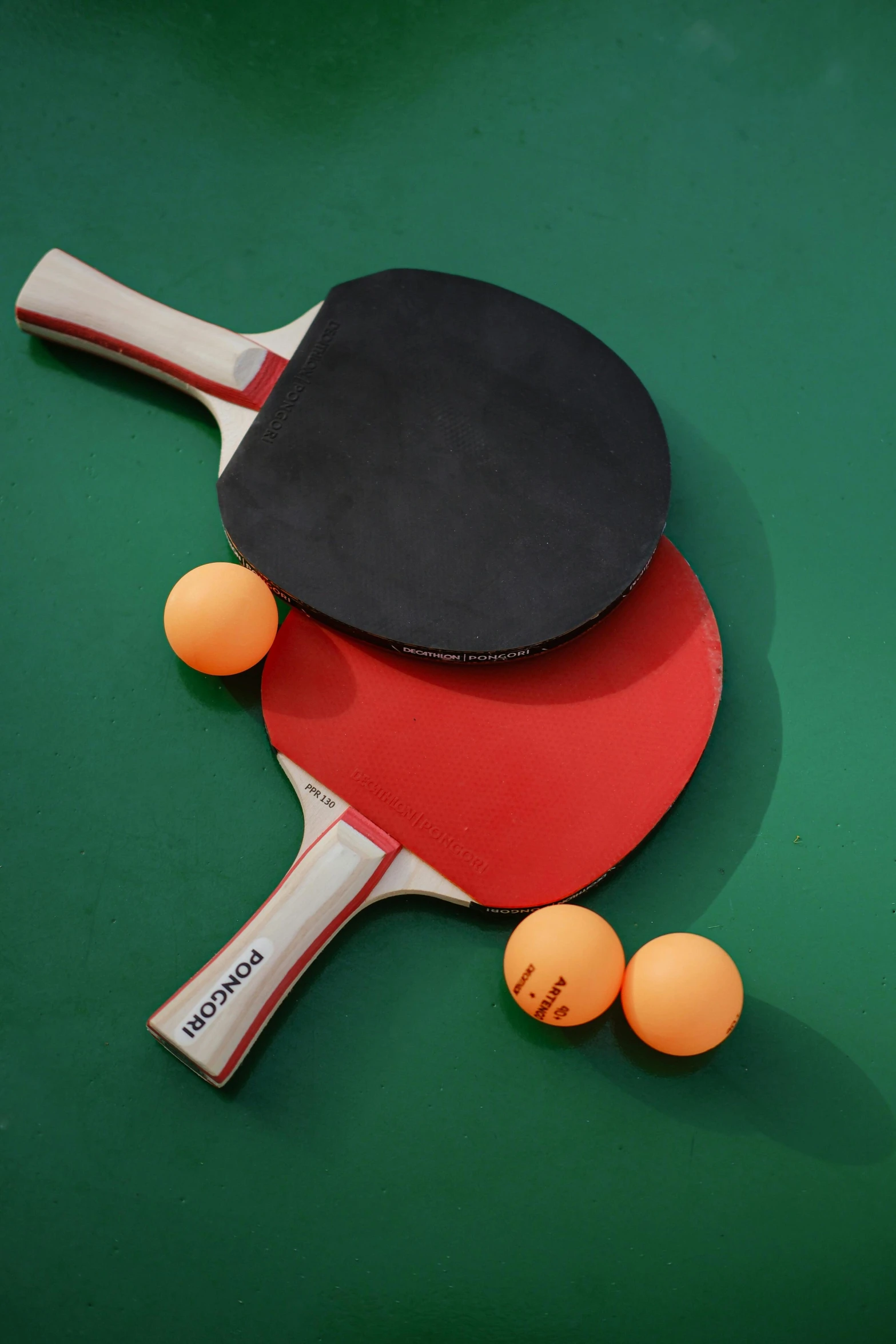 a red and black table tennis paddle resting next to some ping pong balls