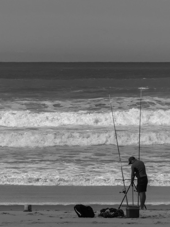 man fishing on the beach while another person stands by the water