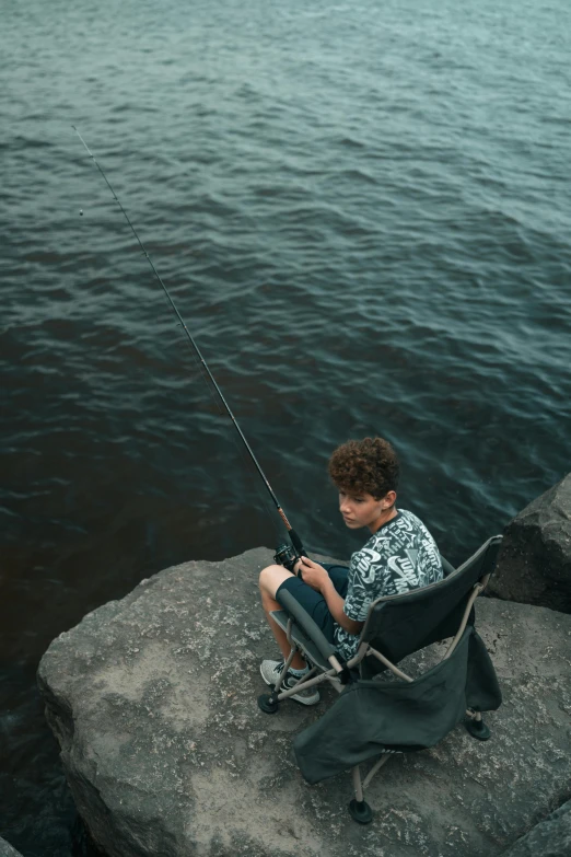 a boy is sitting on rocks by the water