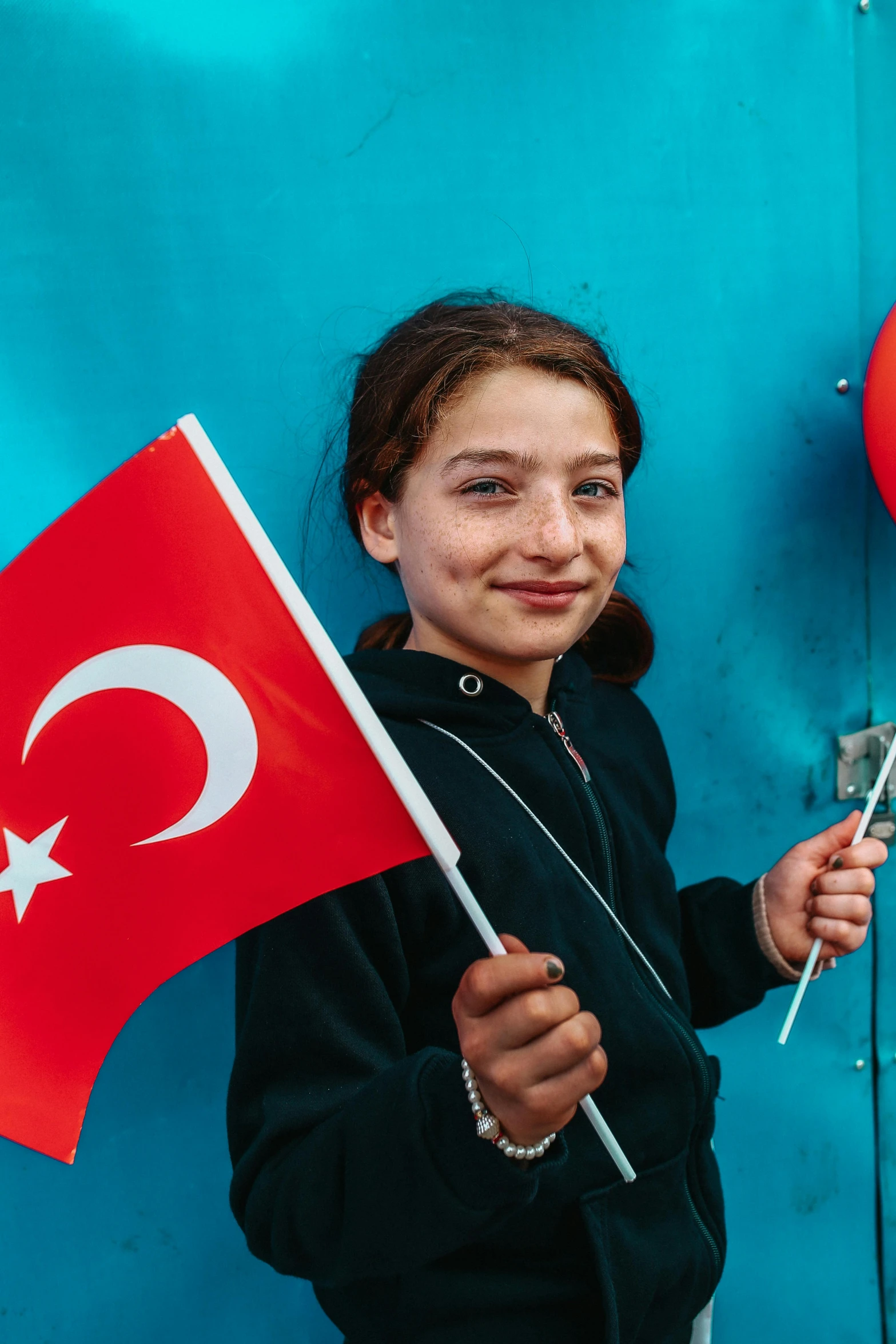 a girl holding a turkey flag poses in front of a blue wall