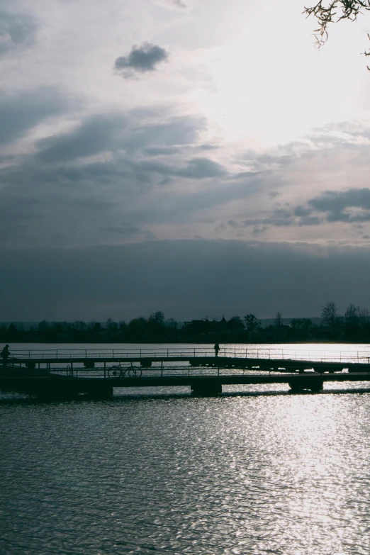 a lake with a boardwalk, trees, and a few people walking across it