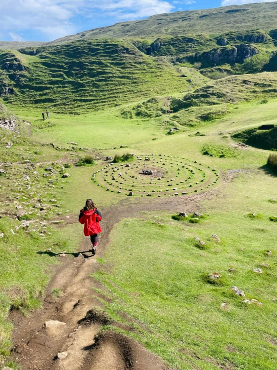 a woman in red coat walking across dirt path in grassy area