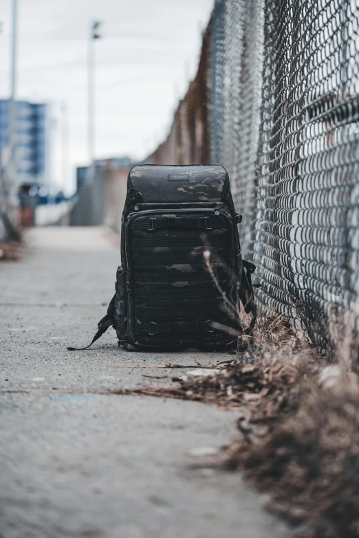 a black backpack is on the ground near a fence