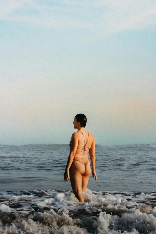a woman standing in shallow water on top of a sandy beach