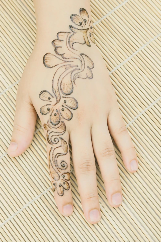 woman's hand with floral temporary tattoo on bamboo mat