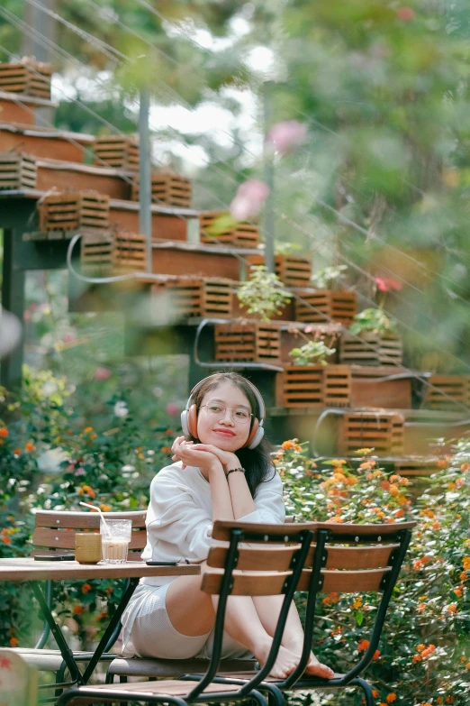 a woman sitting at an outside table in front of a bush