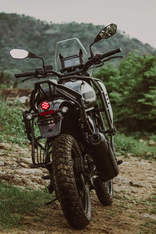 an all black motorcycle with its lights on on a dirt road