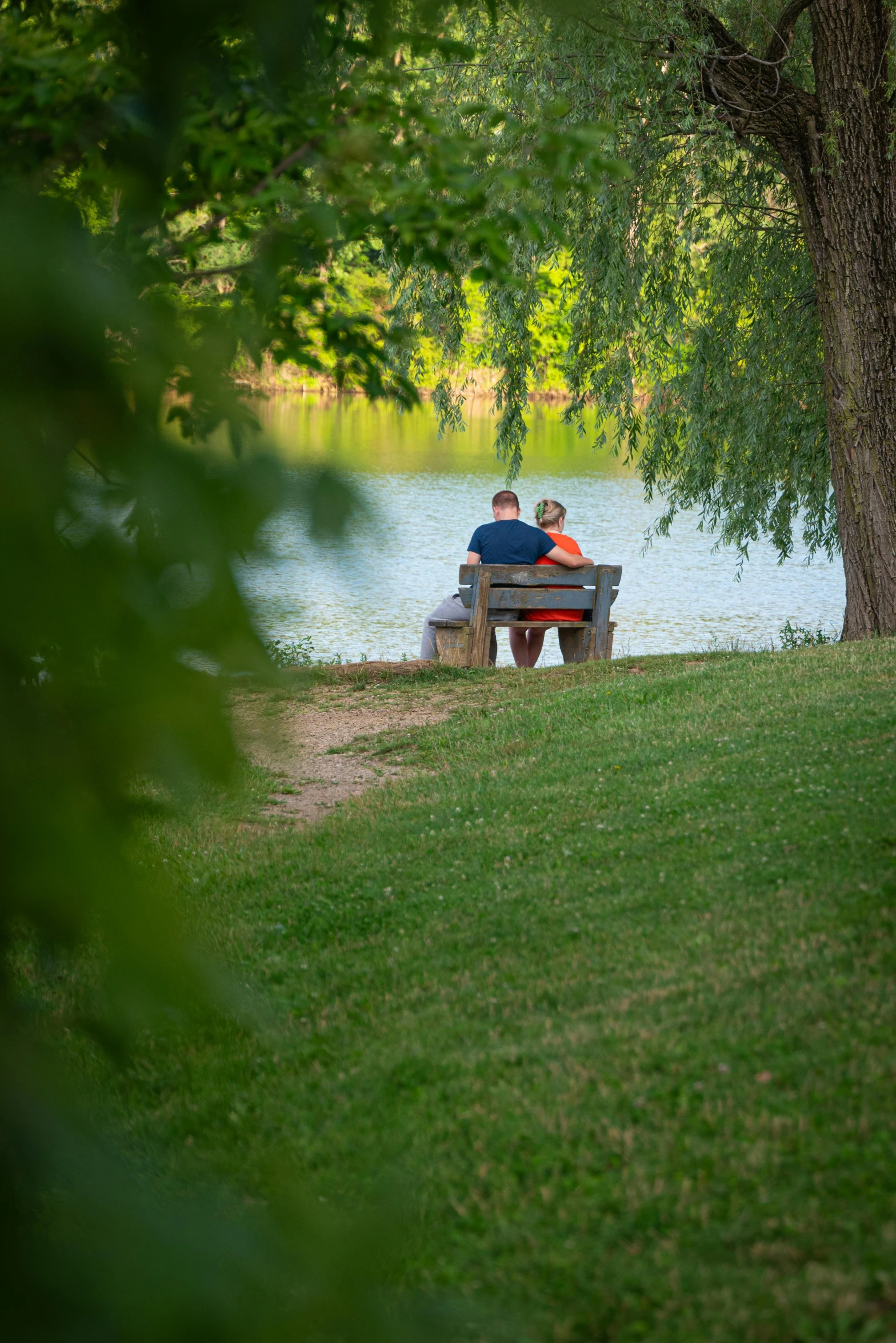 two people sit on a bench in a park near the water