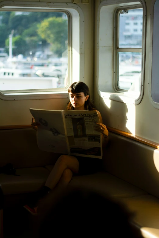 a girl sitting on the seat in a boat reading the paper