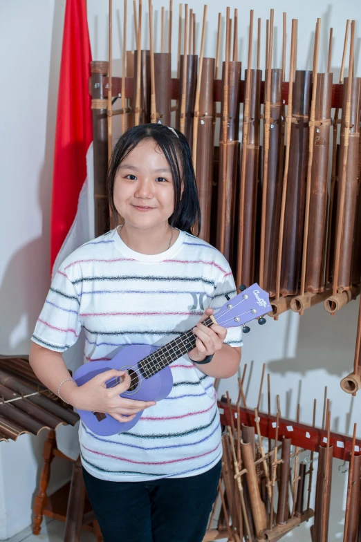 a  holding a ukulele, standing next to a set of musical instruments