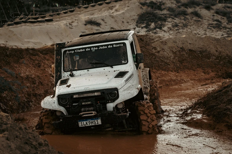 a small white utility vehicle driving through a dle of mud