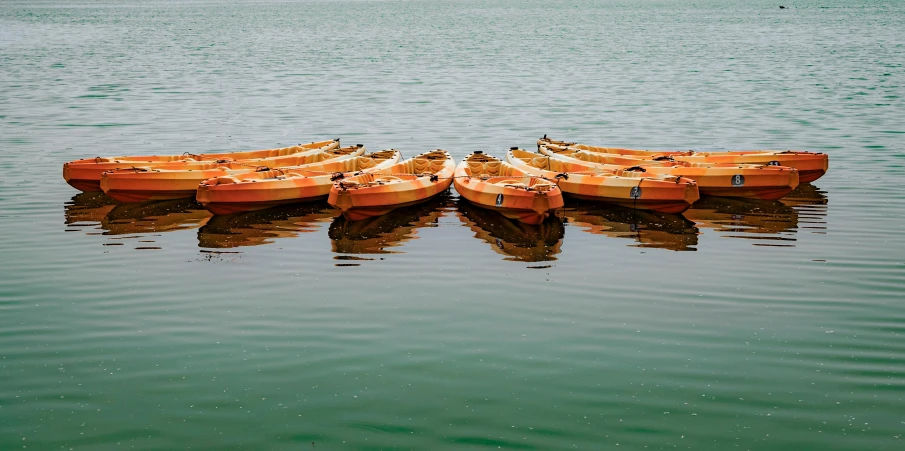three small orange boats on the water with people standing next to them