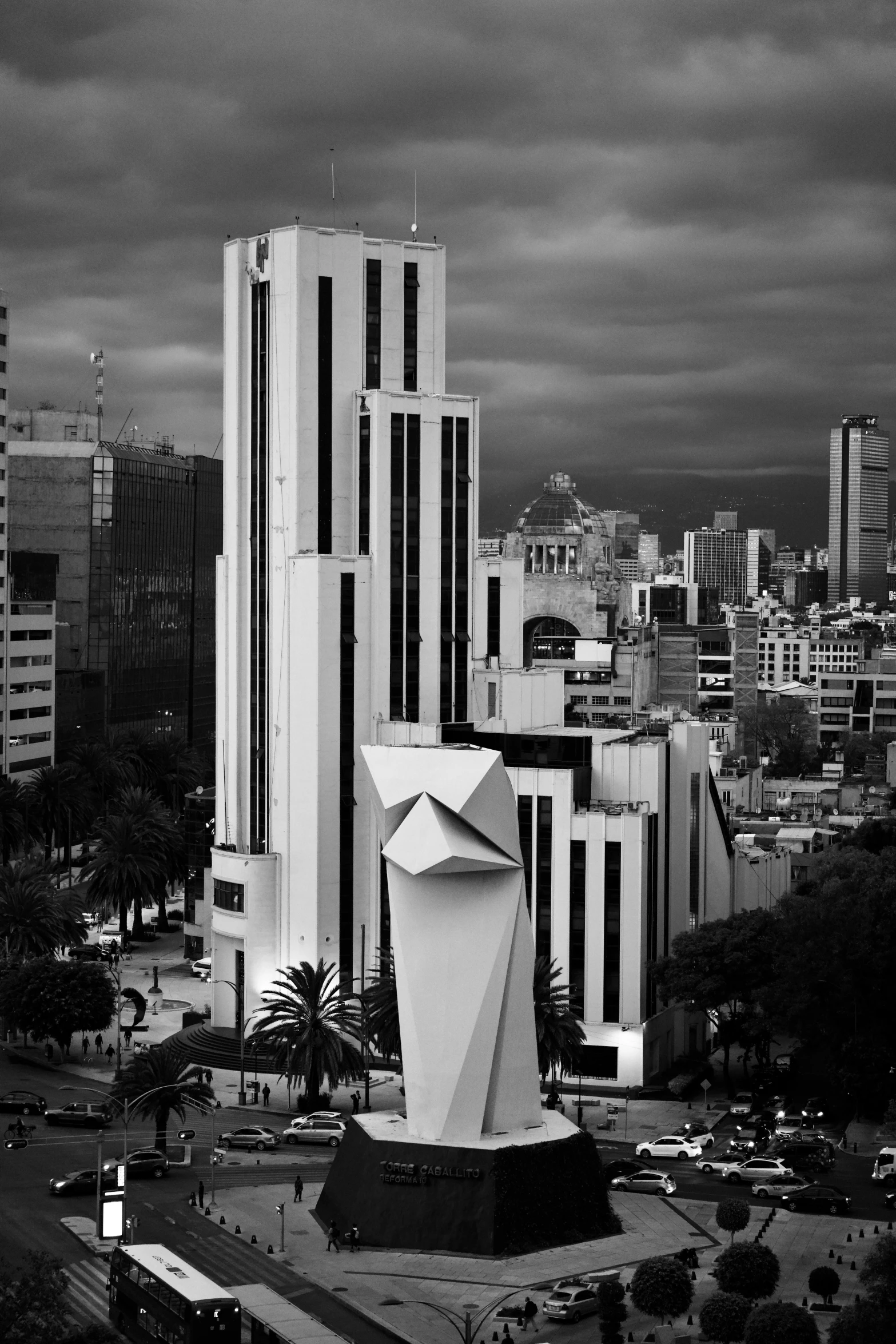 a black and white pograph of tall buildings with an open statue in front of them