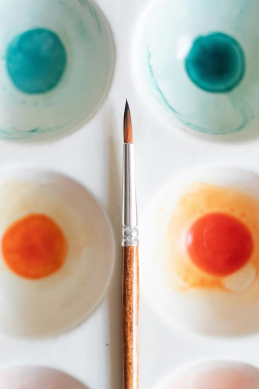 a pencil sits in front of a bowl of colored paint