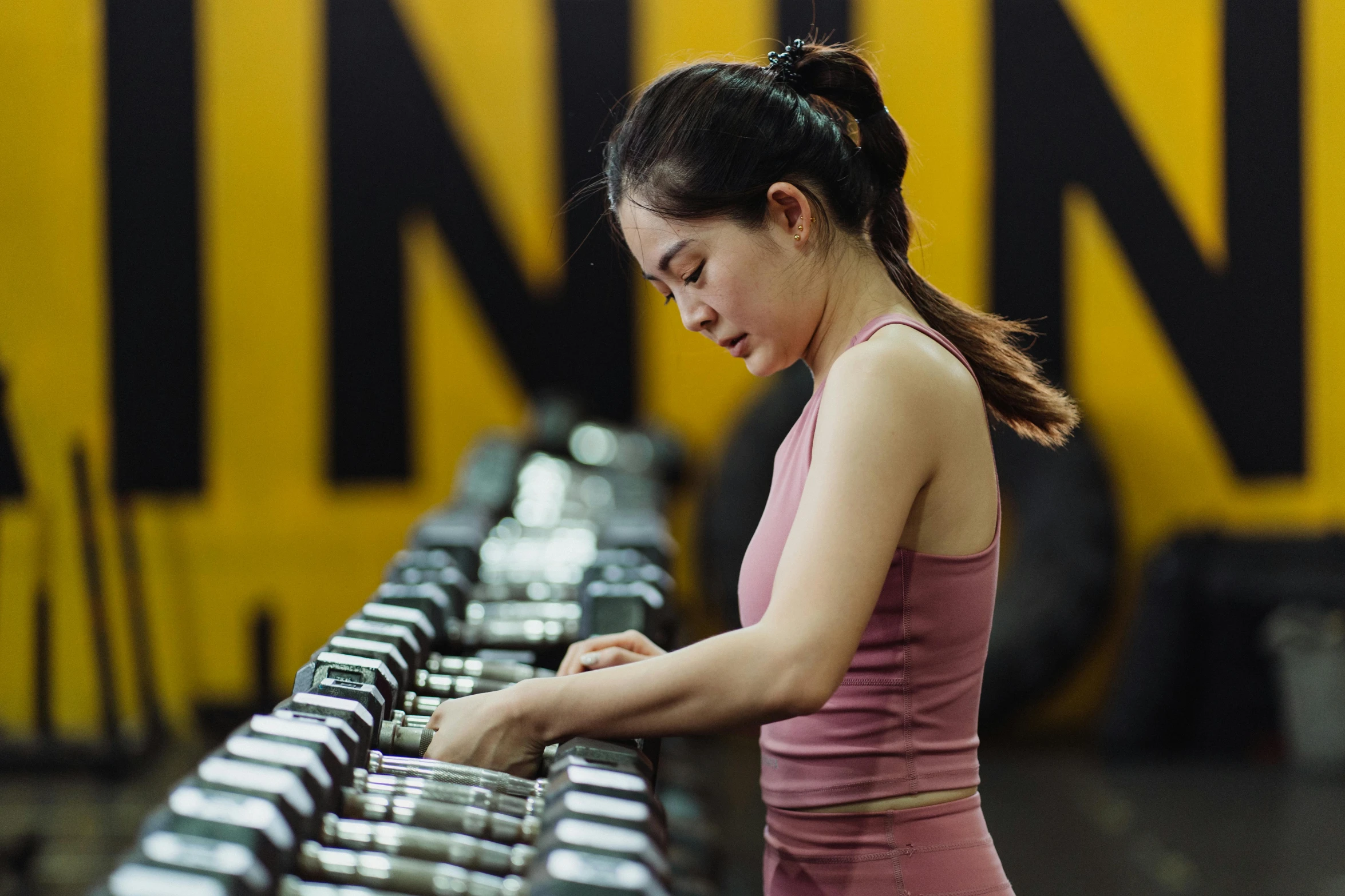 a woman wearing a pink top is standing near dumbs