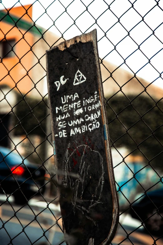 the end of a wooden skateboard is seen through a fence