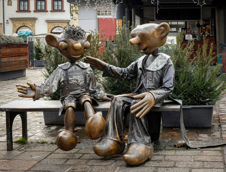 two bronze statue of mice shaking hands while on a bench