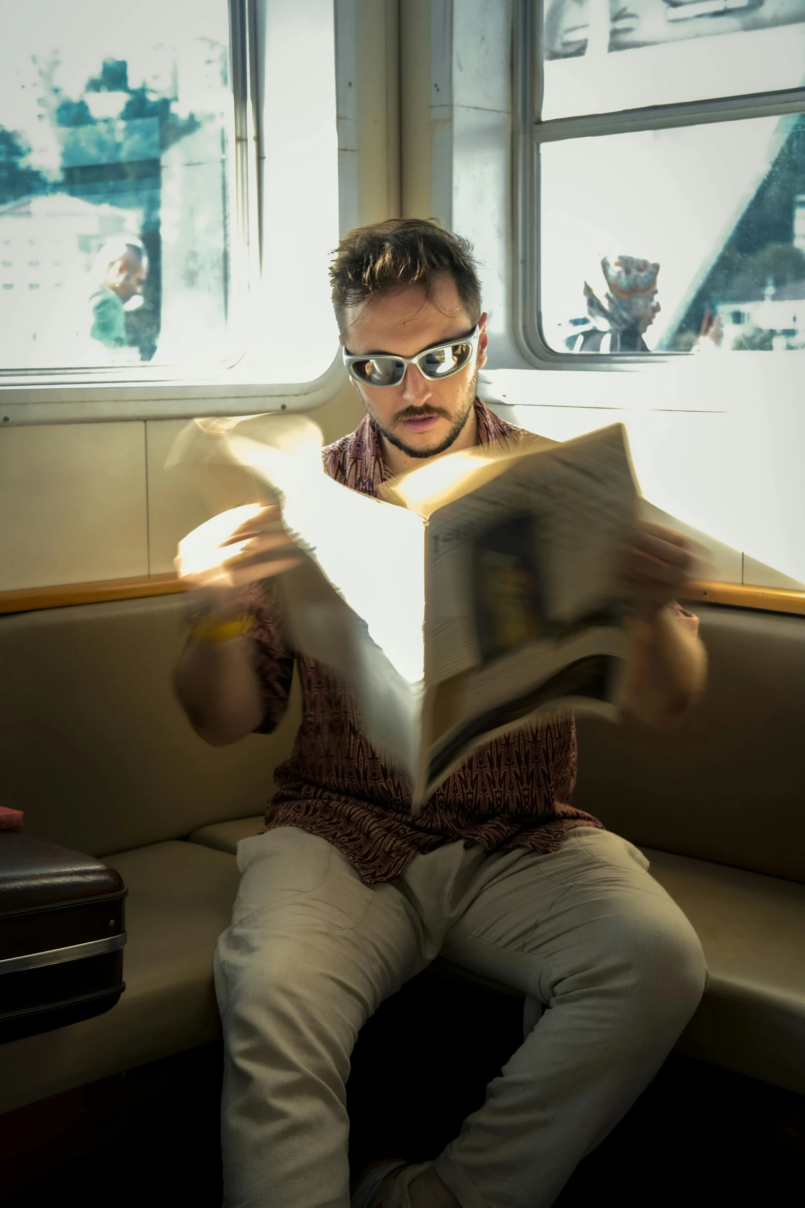 a man sitting down reading a book next to a window